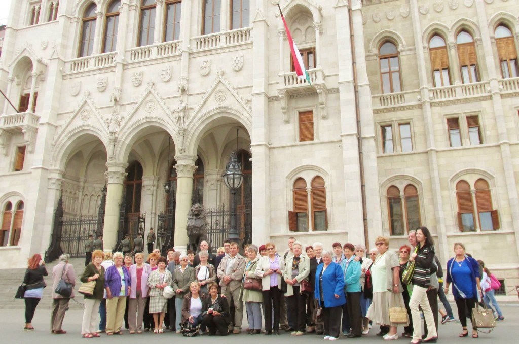 Csoportkép az Esthajnal Nyugdíjas Klub tagjairól a Parlament épülete előtt.